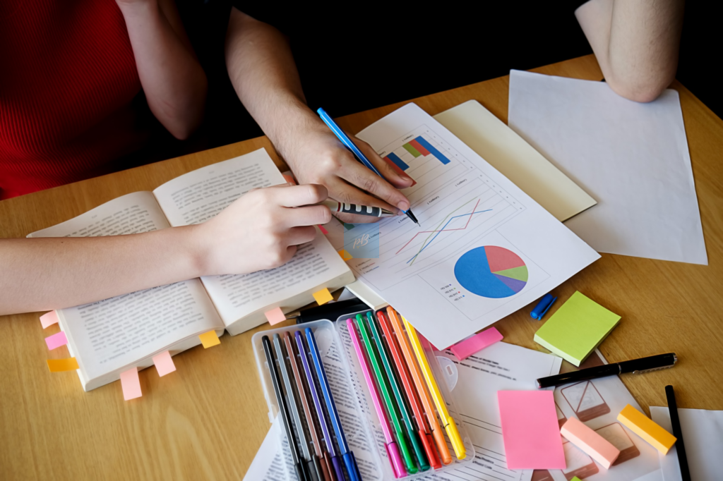 Students analysing graphs and charts with books and colourful stationery as part of a maths school project